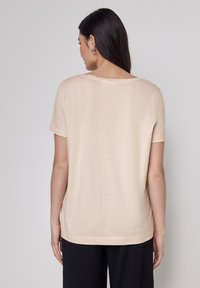 Camiseta de manga corta beige con cuello redondo y un corte relajado. Tela suave y lisa con un detalle de costura mínimo en el dobladillo.