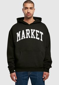 Felpa nera con cappuccio con la scritta "MARKET" in grassetto bianco, tasca a marsupio frontale e cappuccio regolabile con lacci. Vestibilità casual con polsini a coste.