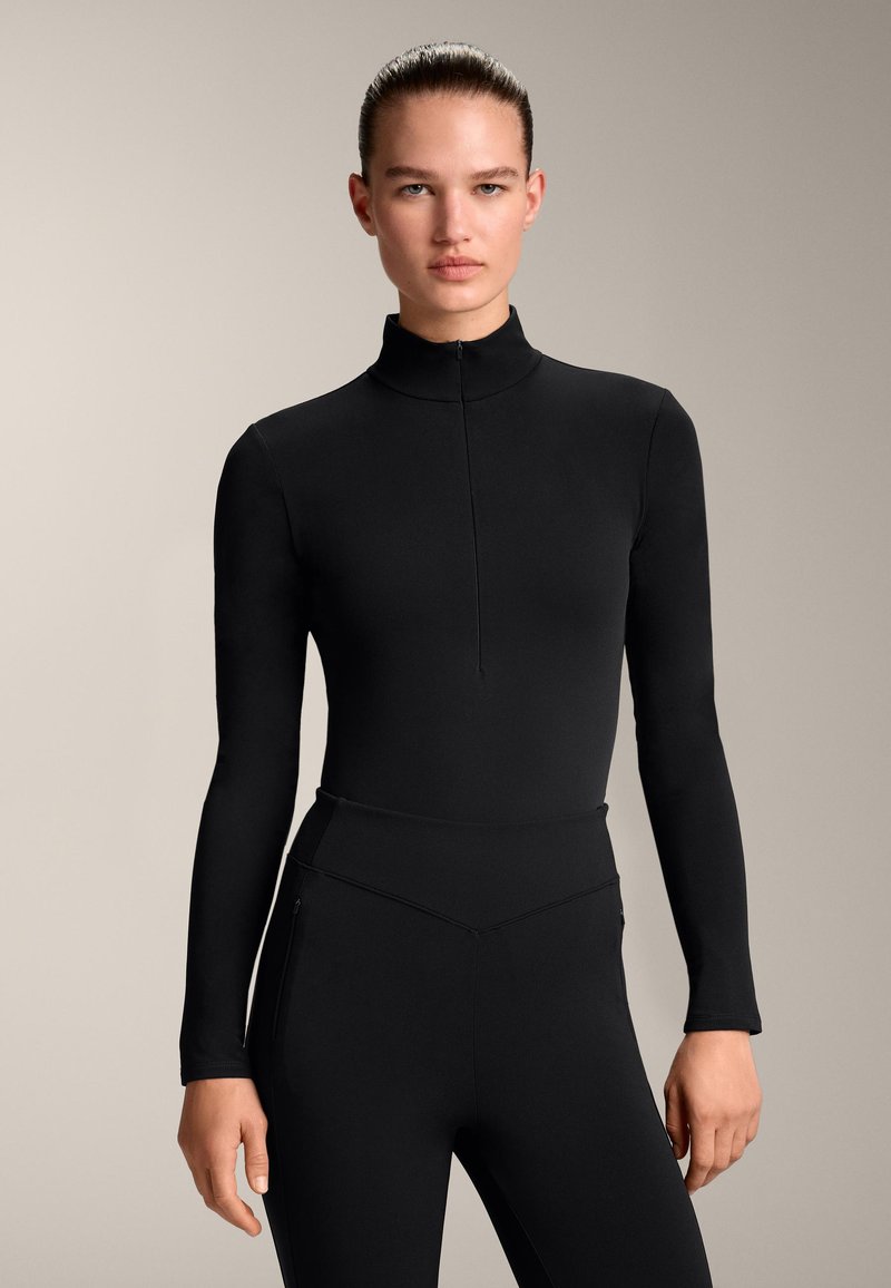 Fekete, hosszú ujjú, cipzáras body magas gallérral; sima textúra és testhezálló kialakítás. Magas derekú nadrággal párosítva.