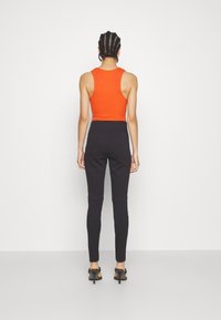 Orange figurerad linne parat med högmidjade svarta leggings, med en elegant design och mjuk textur. Minimalistisk stil utan synliga mönster.