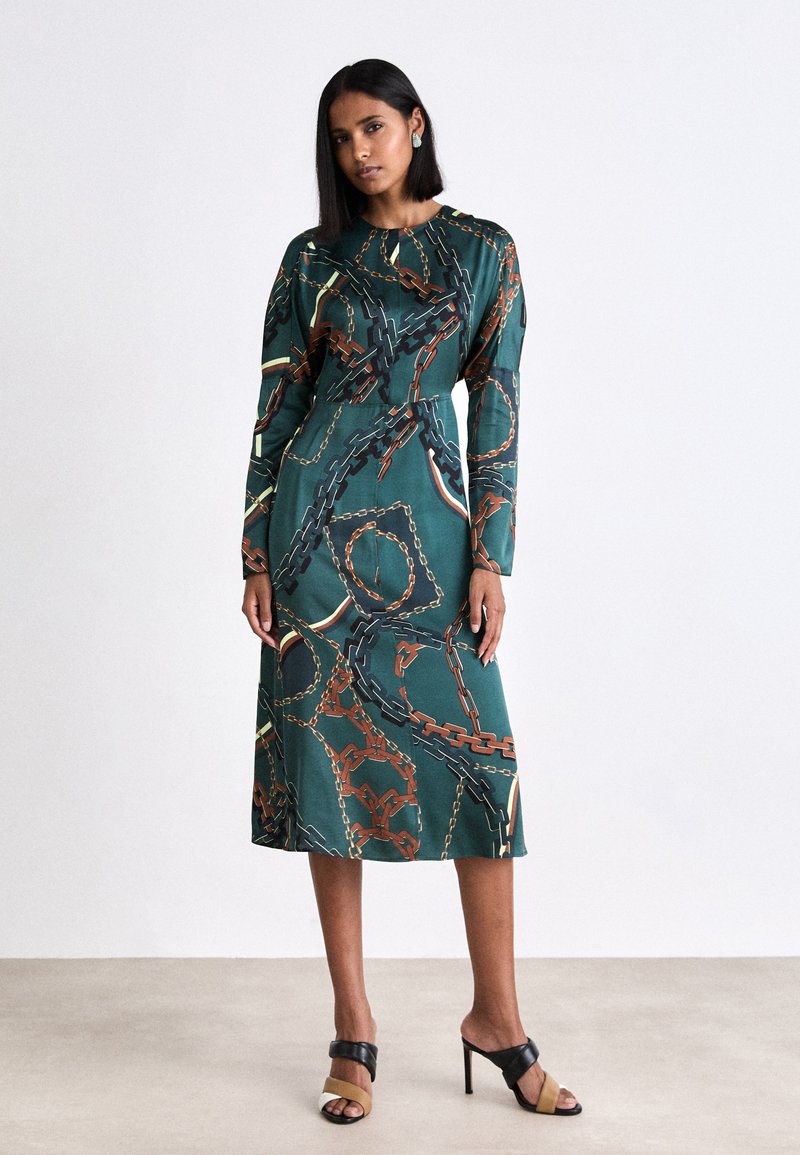 Grünes Kleid mit langen Ärmeln, das ein goldfarbenes und schwarzes Kettenmuster aufweist. Entworfen in einer mittellangen Silhouette mit einer glatten Textur.