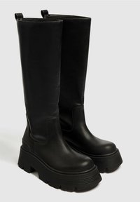Black knee-high boots made of smooth leather, featuring a thick platform sole with a textured tread and pull tabs at the top.