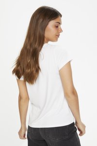 Witte T-shirt met korte mouwen en een ronde halslijn, gemaakt van zachte stof. De achterkant is iets langer, gecombineerd met donkere jeans.