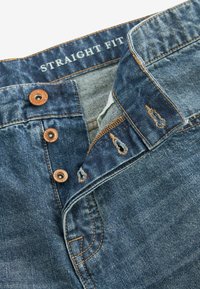 Jeans de mezclilla de corte recto con un lavado azul oscuro, botones de latón y costuras contrastantes. Presenta cierre de botón y patrones de costura visibles.