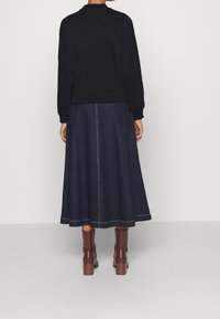 Czarny sweatshirt, denimowa spódnica midi o rozkloszowanym kroju i burgundowe botki za kolano. Spódnica ma kontrastowe przeszycia.