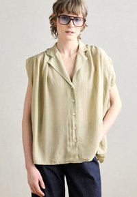 Salvegrønn bluse med korte ermer, lett stoff, krage og knappestolpe foran, kombinert med mørk denimjeans.