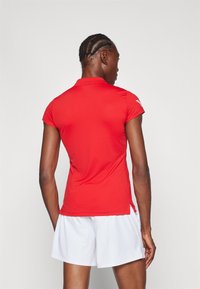 Rode polo met korte mouwen en een gestructureerde stof, voorzien van een platte kraag en zij splitten, gecombineerd met witte shorts.