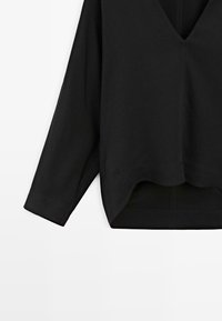 Top nero a maniche lunghe con scollatura a V profonda, caratterizzato da una vestibilità ampia, una trama liscia e un orlo rotondo. Realizzato in tessuto morbido e traspirante.