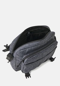 Mochila de tela gris con múltiples compartimentos con cremallera, correas ajustables y un forro interior suave. Exterior texturizado con un detalle sutil.