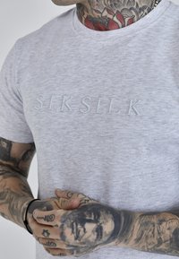T-shirt grigia mélange con colonna a giro, che presenta il logo ricamato "SIKSILK" in azzurro chiaro. Maniche corte, texture morbida, design minimalista.