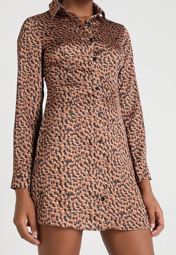 Femme portant une mini-robe marron à manches longues, boutonnée, avec un motif feuille abstrait noir et un col.