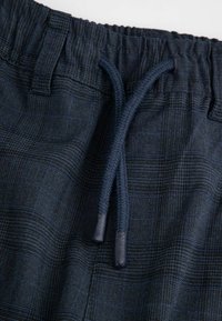 Szorty w granatowy wzór z elastycznym pasem i sznurkiem. Tkanina ma teksturowany, kratkowany wzór w ciemniejszych odcieniach niebieskiego.