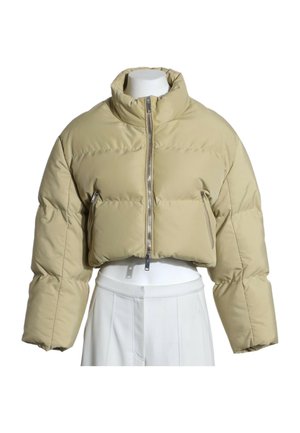 Veste matelassée courte beige à col haut et fermeture éclair frontale, présentée sur un torse de mannequin blanc portant un pantalon blanc.