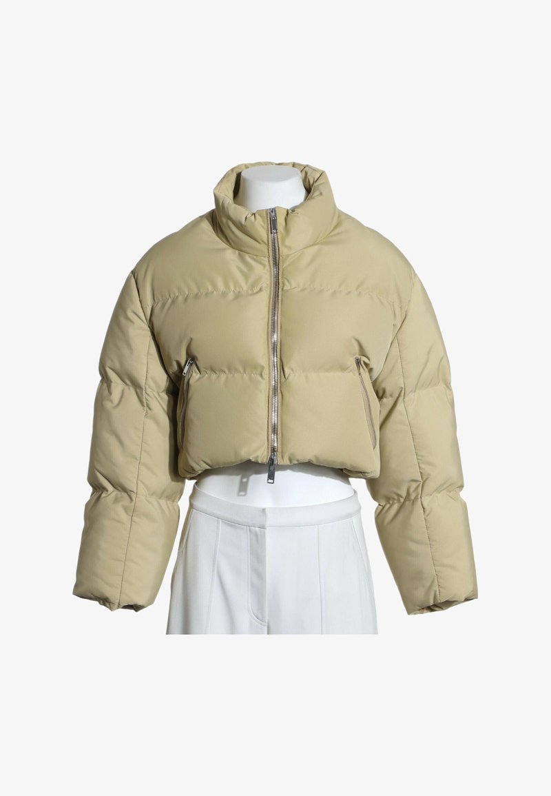 Veste matelassée courte beige à col haut et fermeture éclair frontale, présentée sur un torse de mannequin blanc portant un pantalon blanc.