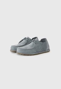 Gray suede shoes with a rounded shape, featuring a low-profile design, stitched detailing, and a textured rubber sole.
