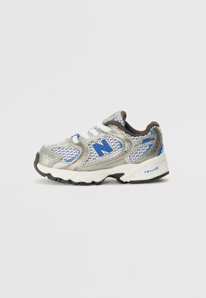 Chaussure de sport enfant grise et blanche avec des accents bleus, tissu en mesh et bride Velcro, vue de côté sur fond uni.