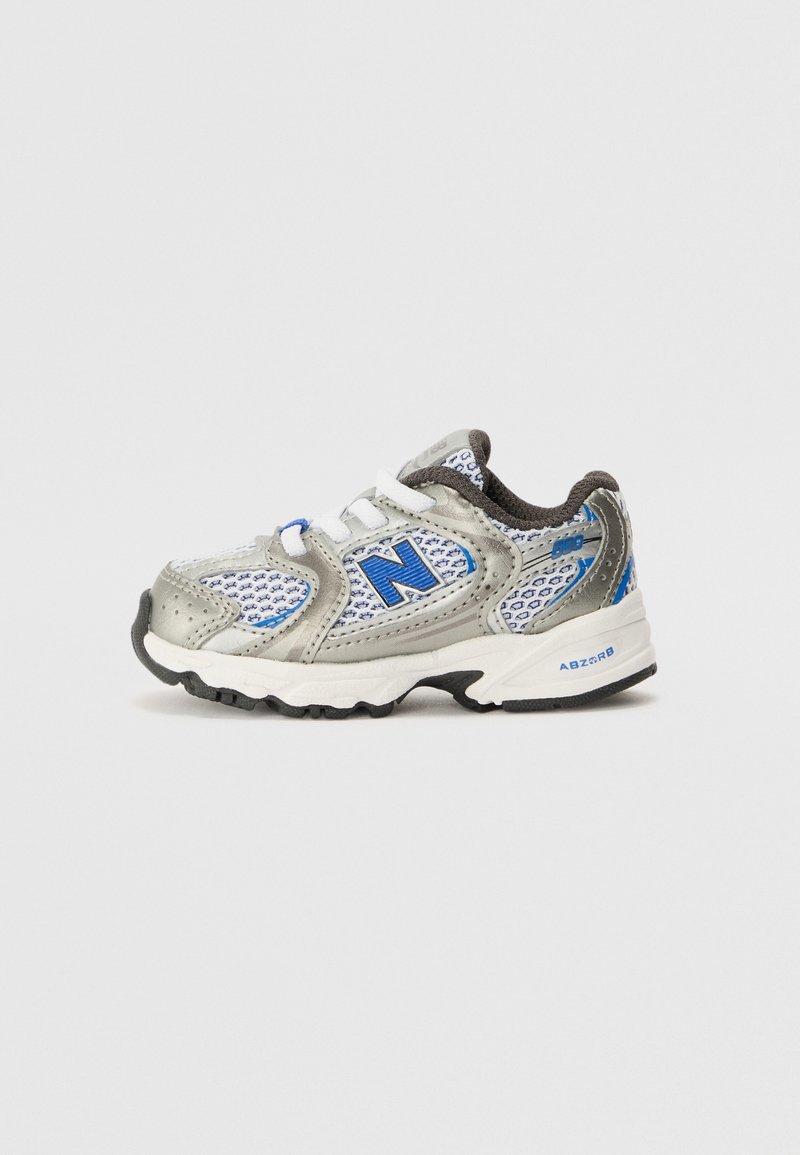 Chaussure de sport enfant grise et blanche avec des accents bleus, tissu en mesh et bride Velcro, vue de côté sur fond uni.