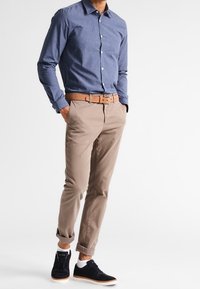 Camisa de botones azul, pantalones caqui, cinturón marrón claro y zapatillas náuticas. La camisa tiene cuello; los pantalones tienen puños. Las zapatillas cuentan con detalles en blanco.