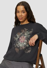 Czarny sweatshirt z graficznym wzorem, który łączy geometryczny motyw z kwiatowymi elementami w delikatnych kolorach. Wykonany z fakturowanej tkaniny.