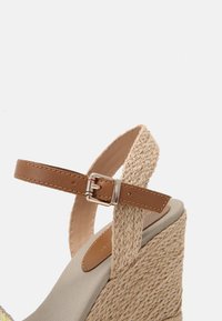 Brun læder ankelrem med en sølvspænde, vævet jute kilehæl, beige tekstilfodbed og glat, afrundet tådesign.