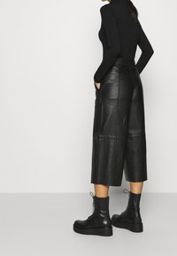 Svarta läderculotter med hög midja, vida ben och sömlös framsida. I kombination med svarta snörda kängor.