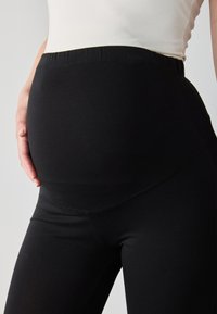 Juodos nėštumo legging kelnes su tampriu juosmeniu, suprojektuotos patogumui, turinčios lygią tekstūrą ir prigludusią siluetą.