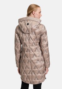 Beige geïsoleerde jas met een capuchon, voorzien van een geometrisch quiltpatroon, lichtgewicht stof en elastische manchetten. Achteraanzicht toont een aangesnoerde zoom.