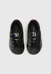 Mustad spordijalatsid tekstureeritud pinnaga, millel on kolm musta triipu, kummist varbakate ja roosad detailid kandadel. Komplektis mustad paelad.