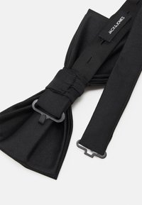 Nœud papillon noir en tissu tissé, présentant une surface texturée et une boucle en métal. Comprend une sangle de marque étiquetée "JACK & JONES".