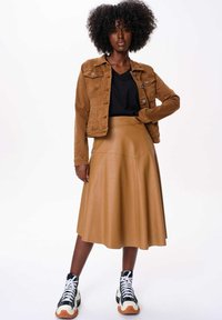 Veste en denim marron, t-shirt noir, jupe en simili cuir beige, et baskets noires avec des détails blancs et orange. Texture lisse, longueur genoux.