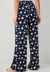 Pantalones de pijama azul marino con un estampado de corazones blancos, confeccionados en un tejido ligero; cuentan con una cintura elástica para mayor comodidad y un corte holgado.