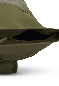 Olívazöld szövet táska cipzáras nyitással, sima textúrával és megerősített varrásokkal. A belső tér fekete, amely mélységet és teret sugall.