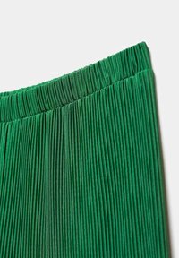 Tissu vert plissé avec une ceinture élastique, montrant de fines plis verticaux et une texture lisse.