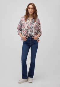 Loose-fitting, multicolored patterned blouse with pink, blue, and gray tones. Paired with dark blue denim jeans and white sneakers.