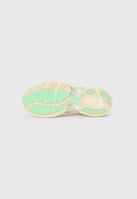 Semelle de sneaker athlétique avec une tige transparente, dotée d'un intermédiaire beige texturé et de accents en caoutchouc vert dans un motif ondulé.