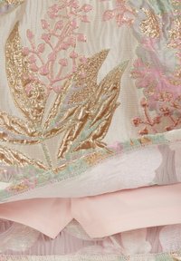Izšūta auduma ar ziedu rakstiem zelta, rozā un zaļā tonī. Gaišs fons ar teksturētu apdari un maigu rozā oderi.