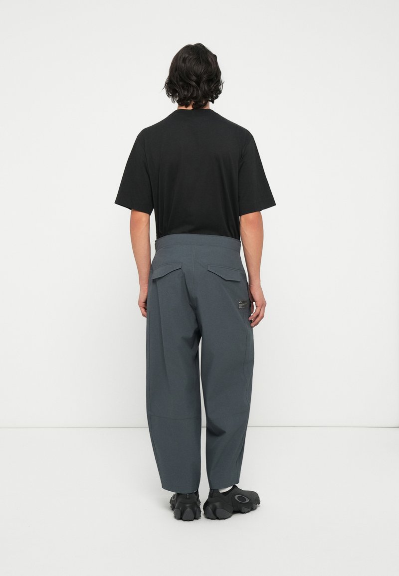 Maglietta nera a maniche corte abbinata a pantaloni grigi larghi con tasche posteriori e una vita testurizzata. Scarpe nere completano l'outfit.