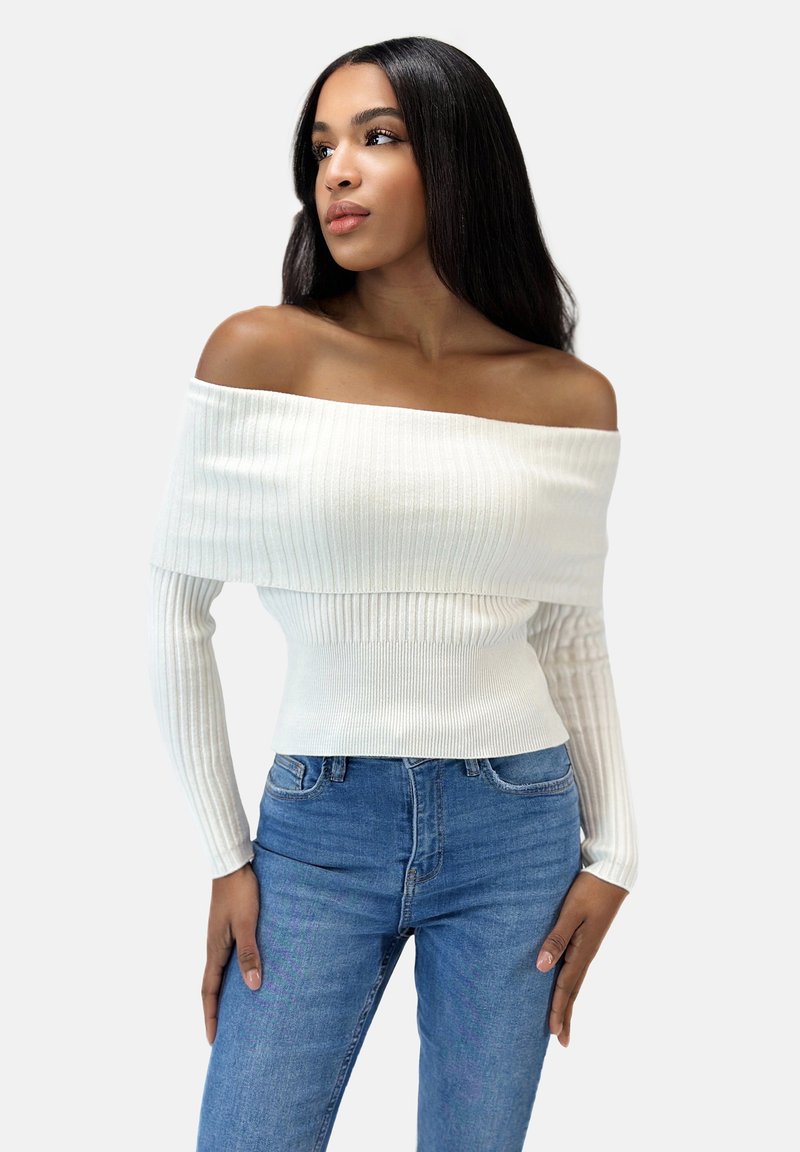 Hvid ribbet off-the-shoulder sweater med lange ærmer, der har en tætsiddende design. Sammen med højtaljede blå jeans.
