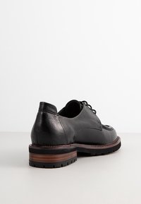 Chaussure en cuir noir avec un bout arrondi, une surface texturée, un laçage étroit et une semelle intermédiaire en bois brun sur une semelle extérieure en caoutchouc noir.