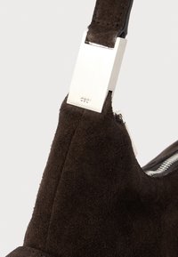 Detailný záber na tmavo hnedú semišovú kabelku so strieborným obdĺžnikovým kovovým uzáverom a viditeľným zipsom.