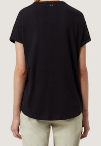 Černé bavlněné tričko s volným střihem, ohrnutými rukávy, kulatým výstřihem a jemnými logy na zadní straně. Hladká textura.