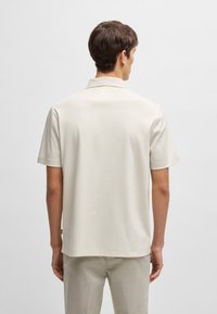 Kortermet polo skjorte i lys beige, glatt stoff, med klassisk krage og rett skjæring. Bakside viser minimal detaljering.