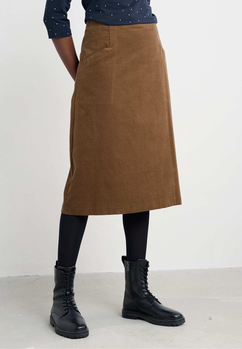 Femme portant une jupe marron longueur genoux, des collants noirs, des bottines noires à lacets et un haut bleu marine à pois blancs.