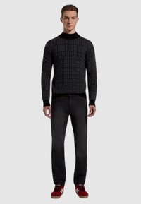 Maglione nero a fantasia con design aderente, colletto e polsini a coste, abbinato a jeans scuri e sneaker rosse. Look semplice e moderno.