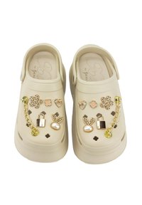 Zuecos beige con diversos accesorios decorativos, incluyendo flores, corazones y formas de conejito, con acentos dorados y un elemento de cadena.