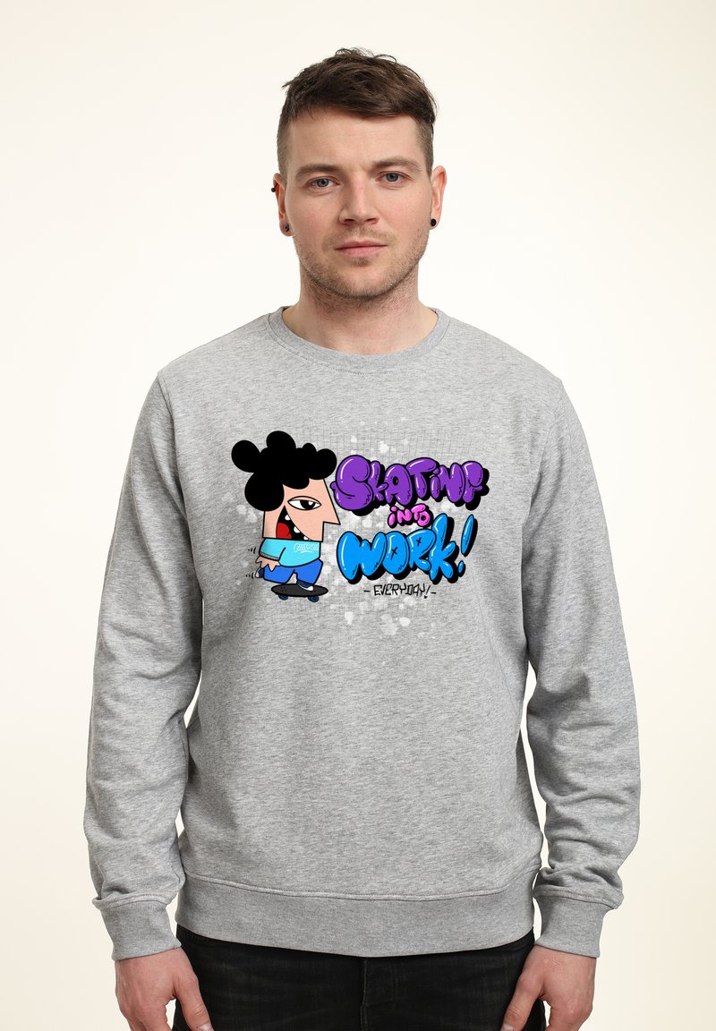 Szary polarowy sweter z kolorową grafiką przedstawiającą kreskówkową postać jeżdżącą na desce z napisem "Skating into Work!" w pogrubionych literach.