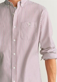 Gestreept overhemd in lichtroze en wit. Voorzien van een borstzak, witte knopen en opgerolde mouwen. Gemaakt van katoen.