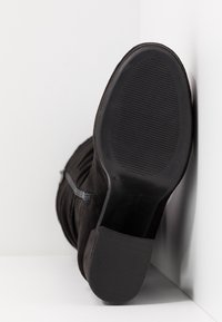 Botín de ante negro con suela de goma texturizada, cremallera lateral y punta redondeada. El tacón tiene una ligera inclinación para mayor estabilidad.