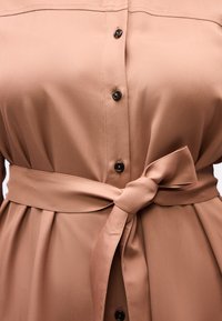 Καφέ φόρεμα με κουμπιά, μαύρα κουμπιά και υφασμάτινη ζώνη δεμένη σε φιόγκο στη μέση.