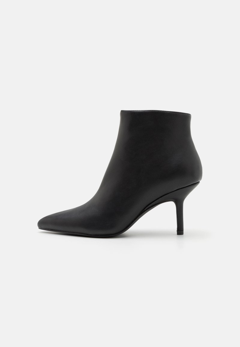 Bottine en cuir noir avec bout pointu et talon moyen fin sur un fond clair uni.